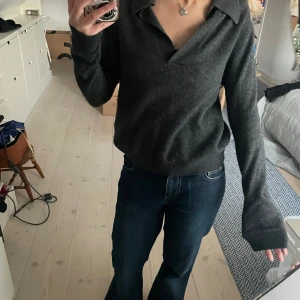 Mörkgrå stickad cashmere tröja med krage  - Mysig mörkgrå stickad tröja  med bred krage och v-ringning. Tröjan har långa ärmar och en avslappnad passform, perfekt för lager-på-lager. Stilren och enkel att matcha till olika outfits.