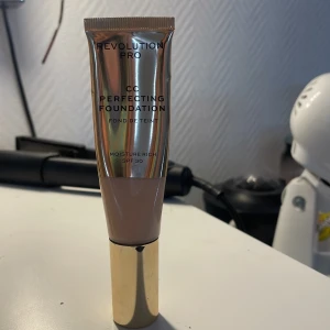 Revolution Pro CC Perfecting Foundation - Revolution Pro CC Perfecting Foundation med SPF 30. Denna fuktgivande foundation ger full täckning och en jämn hudton. Förpackningen är elegant med en guldig kork och en metallisk finish.