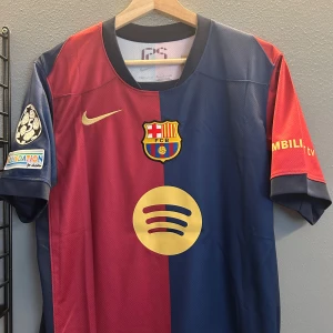 FC Barcelona fotbollströja 2 st lamine yamal - Säljer en FC Barcelona fotbollströja från Nike med korta ärmar. Tröjan har klubbens emblem och sponsorlogga på framsidan. Den är i en klassisk röd och blå design med guldiga detaljer och spelarens namn och nummer på baksidan. 