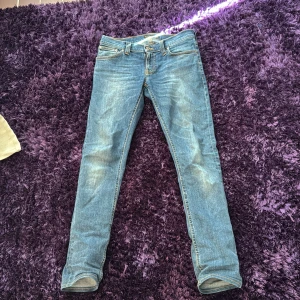 Nudie jeans - Snygga blå jeansbyxor med en klassisk femficksdesign och orange sömmar. De har en slim passform och är perfekta för en avslappnad stil. Midjan är midwaist och byxorna har en dragkedja och knapp framtill.