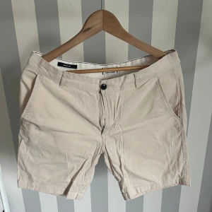 Beige linneshorts från Jack & Jones - Snygga beige linneshorts från Jack & Jones med normal passform. Klassisk design med knapp och dragkedja framtill, bälteshällor och fickor både fram och bak. Perfekta för varma dagar.