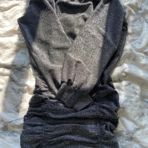 Glittrig svart långärmad klänning - Supersnygg svart glittrig klänning från H&M med långa ärmar. Klänningen har rynkade detaljer längs midjan och ner med en figurnära passform upptill 