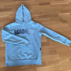 Ljusblå hoodie från Hoodrich - Säljer en ljusblå hoodie från Hoodrich med broderad logga i svart och vitt på bröstet. Tröjan har huva med dragsko och en stor magficka. Perfekt för dig som gillar streetwear och vill ha en snygg och bekväm tröja. Inga defekter. Modellen på bilden är 175 cm lång och väger 64 kg. 