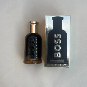 BOSS Bottled Absolu Eau de Parfum 50ml - Säljer en elegant BOSS Bottled Absolu Eau de Parfum i en stilren svart flaska med guldlock. Förpackningen är lyxig med en reflekterande yta och tydlig logotyp. Perfekt för den som vill ha en sofistikerad doft.test spreyad en gång!