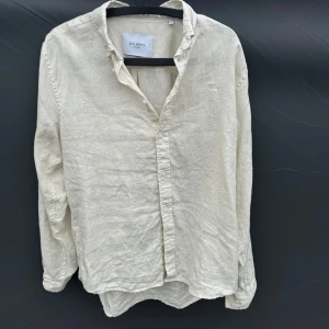 Beige linneskjorta från Les Deux - Säljer en stilren beige skjorta från Les Deux i 100% linne. Skjortan har klassisk krage, knäppning framtill och långa ärmar. Perfekt för en avslappnad men ändå uppklädd look.väldigt bra skick.