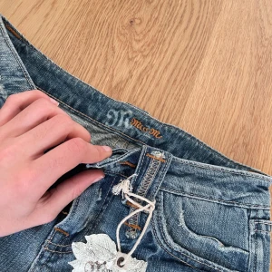 Blå jeansshorts från Miss Me med broderade detaljer - Säljer ett par blå jeansshorts från Miss Me med snygga slitningar och broderade detaljer på bakfickorna. De är nya med lapp och köptes i USA för 60$ se bild 2. MAN KAN KLIPPA DE OM MAN INTE VILL ATT DE SKA VARA SÅ LÅNGA. Pris kan diskuteras.