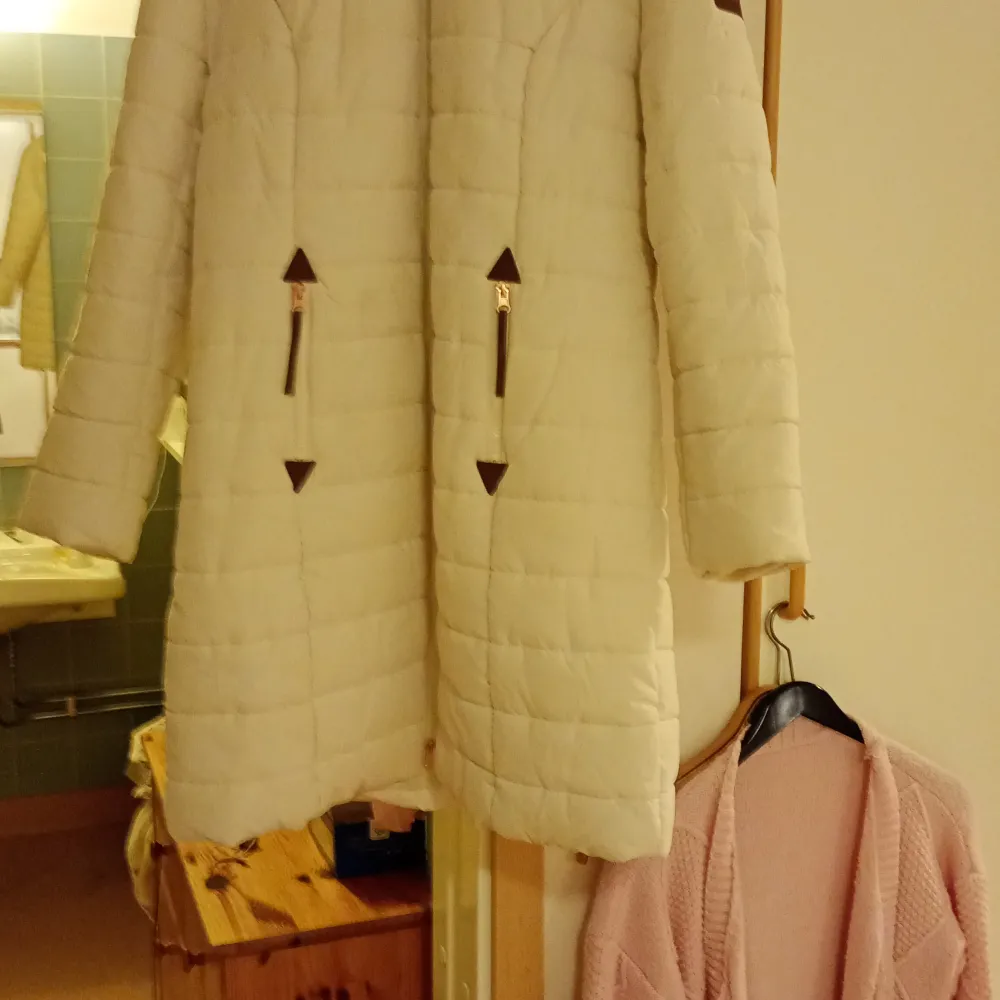 Säljer en stilren vit quiltad kappa med långa ärmar och huva. Kappan har dekorativa detaljer i form av bruna knappar och dragkedjor framtill. Perfekt för kyliga dagar.stl 42/44. Takit.
