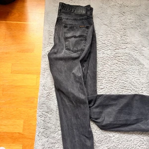 Svarta jeans från Nudie Jeans - Snygga svarta jeans från Nudie Jeans med klassisk femficksdesign och subtila broderade detaljer på bakfickan. Perfekta för en stilren look. Model: Rad Rufus Färg: Vintage black