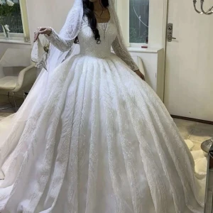 Vit bröllopsklänning - Elegant vit bröllopsklänning med glittrande detaljer och spets. Klänningen har långa ärmar och en vid kjol som ger en klassisk prinsesskänsla. Perfekt för den stora dagen! Behöver kemtvättas så blir den helt perfekt! Den är specialbeställd från Berlin. 