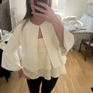 Vit kavaj från Esprit - Säljer en vit kofta med volangdetaljer vid ärmslut och midja. 