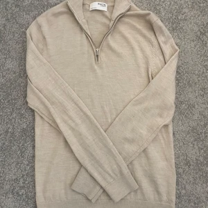 Beige merinoulltröja med halv dragkedja från Selected Homme - Säljer en stilren beige långärmad tröja från Selected Homme i mjuk merinoull. Tröjan har halv dragkedja vid halsen och ribbade muddar. 