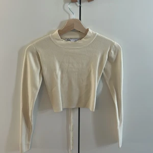 Beige croppad topp från Zara - Säljer en beige croppad topp från Zara med lång ärm och öppen rygg med knytband. Toppen är ribbad och har en snygg, enkel design som passar perfekt till många outfits. 💛