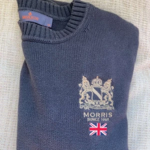 Mörkgrön stickad tröja från Morris - Säljer en mörkgrön stickad tröja från Morris med broderad logga och brittisk flagga på bröstet. Tröjan har rund halsringning och långa ärmar med ribbade muddar. Endast 349kr