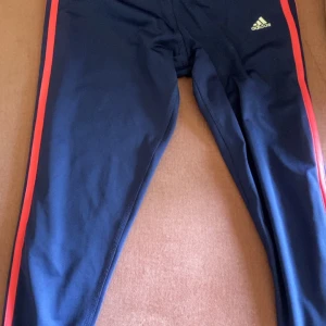 Y2k träningsleggings från Adidas  - Y2k Mörkblå träningsleggings från Adidas med rosa ränder längs sidorna och låg midja . Byxorna har en tight passform och är perfekta för träning. Snygga och sportiga tights som sitter skönt.