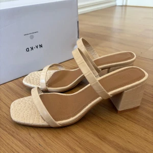 Beige sandaler med klack från NA-KD - Snygga beige lågklackar från NA-KD. Perfekt till sommaren! Helt oanvänd, endast testad. 