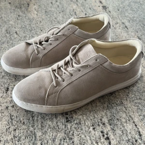 Beige sneakers från Jack & Jones - Säljer ett par stilrena beige sneakers från Jack & Jones. Skorna har ovandel i mocka, vita gummisulor och klassisk snörning. Perfekta för dig som gillar en clean och enkel look.