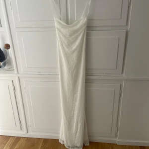 Vit långklänning med spets och smala axelband - Säljer en elegant vit långklänning med smala axelband och vacker spetsdetalj. Klänningen har en rak passform och knytning i ryggen för extra detalj. Perfekt för sommarens speciella tillfällen.