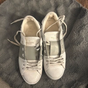 Valentino Garavani Open sneakers i vitt och grönt - Säljer ett par snygga Valentino Garavani Open sneakers i vitt skinn med bred ljusgrön rem över mitten. Klassisk rund tå, vita snören och diskret logga på plösen. Perfekta för dig som gillar stilrena och exklusiva sneakers. Använt skick🫶Är 37 1/2 men funkar för mig som har 38