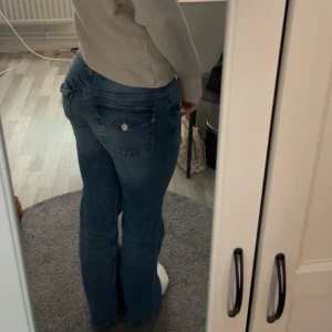 Blå bootcut jeans  - Säljer ett par blå bootcut jeans med snygga detaljer på bakfickorna och. Jag skulle säga att de är lågmidjade men beror på vilken kroppstyp man har 🫶🏻