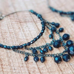 Svarta glittriga örhängen - Säljer ett par stora örhängen med svarta glittriga pärlor och kedjor. Örhängena har flera lager av kedjor och pärlor som hänger i olika längder för en cool och unik look.