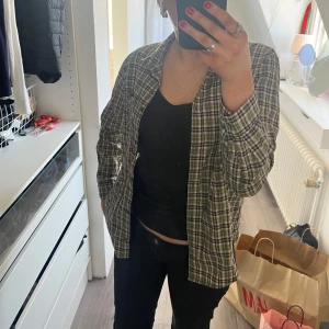 Rutig skjorta från Monki - Säljer en snygg rutig skjorta från Monki i gröna, svarta och röda toner. Skjortan har långa ärmar och en klassisk krage. Perfekt för en avslappnad stil.