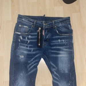 Blå Dsquared2 jeans med unik detalj - Snygga blå Dsquared2 jeans med slitningar. De har en dragkedja och knapp framtill. Perfekta för en avslappnad stil med en twist. Pris 700kr. Passar dig som är ish 170-175 lång. Kom privat för mer bilder eller mer info. Vid en snabb affär kan priset påverkas.