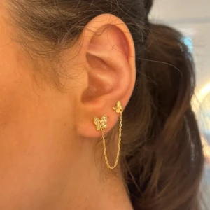 Guldörhängen med fjäril och kedja - Eleganta guldörhängen med en fjärilsdesign och en tunn kedja som kopplar ihop dem. Perfekt för att ge en unik touch till din stil. De är från Glitter och i 18K guld, knappt använda.