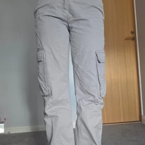 Grå cargobyxor - Säljer ett par grå cargobyxor med flera praktiska fickor på sidorna. Byxorna har en avslappnad passform och är perfekta för en casual look. De är tillverkade i ett slitstarkt material och har en klassisk design.