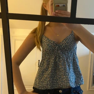 Blommig topp från design by si - Supersöt blå linnetopp med små vita blommor. Toppen har smala axelband, knyt framtill och lätt rynkad midja och rygg. Perfekt för varma dagar och enkel att matcha med jeans eller kjol.  Hör av dig vid frågor eller interesse💞