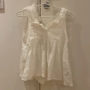 Volangtopp från Ginatricot - Säljer en söt vit linnetopp från Gina Tricot med volangdetaljer vid axlarna och lös passform. Toppen har en söt rosett på ryggen. Har bara använt en gång. Priset kan diskuteras💕