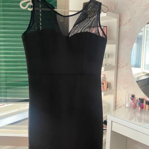 Svart ärmlös klänning med mesh-detalj - Säljer en svart, tight klänning med ärmlös design och mesh upptill som ger en snygg och modern look. Perfekt för dig som vill ha en stilren och elegant outfit.