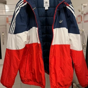 Färgglad vindjacka från Adidas - Säljer en retroinspirerad täckjacka från Adidas i blått, vitt och rött. Jackan har huva, dragkedja och klassiska Adidas-ränder på axlarna. Perfekt för dig som gillar sportig stil och vill sticka ut 150 kr. Röd hoodie 110 kr, rosa hoodie 110 kr, svart tröja 100 kr, hoodie med dragkedja 135kr