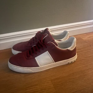 Valentino flycrew vinröda storlek 43 - Snygga sneakers från Valentino i rött och vitt skinn. Skorna har en klassisk design med snörning och en vit sula. Perfekta för en stilren look. Storlek 43 alla nitar förutom en finns kvar och det har blivit en skada där den ska sitta som man ser på sista bilden. Priset går att diskutera vid snabb affär!! 