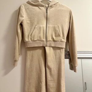 Beige velour hoodie och byxor - Säljer en mysig beige hoodie med dragkedja och matchande byxor i mjukt velourmaterial. Hoodien har långa ärmar och en praktisk huva. Perfekt för en avslappnad stil.