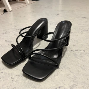 Svarta sandaletter - Snygga svarta sandaler med klack och smala remmar. De har en fyrkantig tå och en stilren design som passar lika bra för en kväll ute som till jeans. Klacken är stabil och ger bra höjd utan att kompromissa med komforten. Aldrig använda då jag har för många..