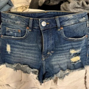 Blå jeansshorts med slitningar och fransar - Säljer ett par blå jeansshorts med slitna detaljer och fransig kant. Shortsen är väldigt fina och användbara💗💗
