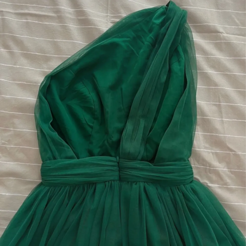 Säljer en elegant grön långklänning med oneshoulder och markerad midja. Klänningen har ett vackert fall i tyget. Perfekt för bal eller festliga tillfällen. Den är använd en gång och går till marken på mig som är 173cm midjemått är 35,5cm. Mekot.