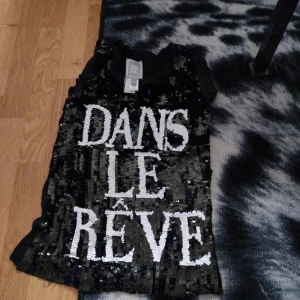 Svart paljettlinne med text från Y.A.S - Säljer ett svart linne från Y.A.S täckt av svarta och vita paljetter med stor vit text 'DANS LE RÊVE' framtill. Linnet har ärmlös design och rund halsringning. Perfekt för dig som vill sticka ut med en glittrig look.