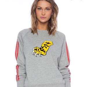 Marc by Marc Jacobs Sweatshirt Tiger, Tiger Paw Sweatshirt - Säljer en grå sweatshirt med ett coolt gult och svart tigertryck på framsidan. Tröjan har röda ränder längs ärmarna och en rund halsringning. Perfekt för en avslappnad stil!