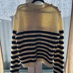 Vit och svart randig stickad tröja med knappar på axeln - Mysig stickad tröja i vitt och svart med breda ränder och dekorativa guldknappar på ena axeln. Från Zara !! Använd 1 gång ❣️köpte den i Xl för en oversized look ❣️