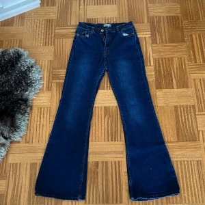 Blå bootcut jeans från Wite & Black - Snygga mörkblå bootcut jeans från Wite & Black med klassisk femficksdesign och gylf med dragkedja. Jeansen har hög midja och är tillverkade i mjukt denimtyg som sitter skönt. Perfekta för dig som gillar en retroinspirerad look.