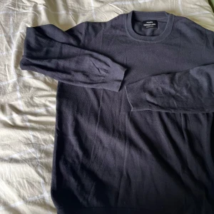 Svart stickad tröja från Mads Nørgaard - En svart stickad tröja från Mads Nørgaard med rund halsringning och långa ärmar. Enkel och stilren design som funkar till allt. Mjuk och skön känsla, perfekt för lager-på-lager under kyliga dagar.