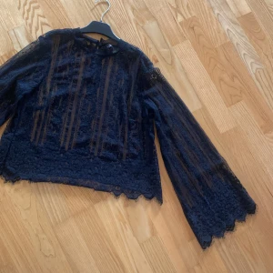 Svart spetsblus med vida ärmar - Supersnygg svart blus i transparent spets med långa, vida ärmar och fina spetsdetaljer längs kanterna. Blusen har rund halsringning. Siper snygg att ha ett svart linne eller svart bh under 