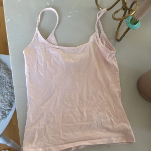 Ljusrosa linnetopp med smala axelband - Enkel och stilren ljusrosa linnetopp med smala axelband. Perfekt att matcha med jeans eller kjol för en avslappnad look. Mjuk och skön känsla mot huden.