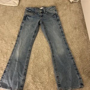 Bootcut jeans från Gina Tricot - Snygga ljusblå bootcut jeans från Gina Tricot i klassisk denim. Jeansen har fem fickor, coola bakfickor med lock och knapp, samt slitna detaljer för en avslappnad vibe. Perfekta för dig som gillar retrostil och vill ha ett par jeans med lite extra attityd.