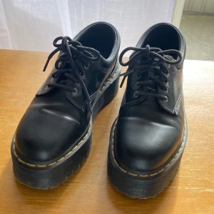  Dr. Martens 8053 - Klassiska svarta Dr. Martens med kraftig platåsula och ikoniska gula sömmar. Skorna har rund tå, snörning och är tillverkade i skinn. Perfekta för dig som vill ha en edgy och tidlös look med extra höjd. Litet märke på höger sko, inget som syns.