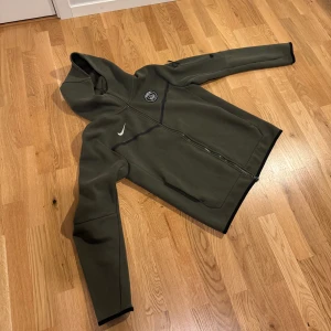Olivgrön PSG hoodie från Nike - Snygg olivgrön hoodie från Nike med PSG-logga på bröstet och hel dragkedja. Tröjan har huva, svarta detaljer och fickor framtill samt en extra ficka med dragkedja på ärmen. Perfekt för dig som gillar sportig stil och vill sticka ut. Knappt använd 8/10 skick 