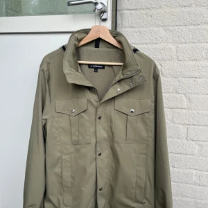 Beige vindjacka från J.Lindeberg L - Snygg beige vindjacka från J.Lindeberg i storlek L. Jackan har raka linjer, två bröstfickor med lock och knappar, samt dragkedja och tryckknappar framtill. Perfekt för vår och höst. Enkel och clean stil som funkar till det mesta. Alldrig använt! Nyskick