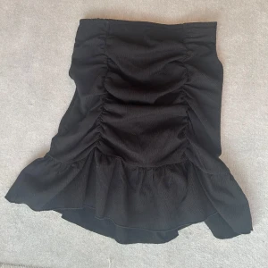 Svart volangkjol från Gina Tricot XS - Supersnygg svart kortkjol från Gina Tricot i storlek XS. Kjolen har volang nertill och snygga rynkade detaljer framtill som ger en cool och trendig look. Perfekt att styla med en croppad topp eller oversized hoodie.