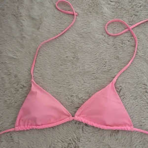 Rosa bikiniöverdel med snörning - Snygg rosa bikiniöverdel i klassisk triangelmodell med tunna snören som knyts i nacken och ryggen. Perfekt för stranden eller poolen, enkel och stilren design som ger en fräsch look. Materialet känns mjukt och följsamt mot huden.